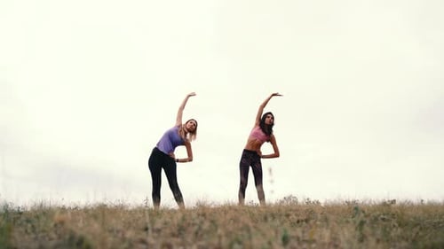 Two Young Fitness Woman Doing Exercises on the Gym in an Outdoor on the Sky Background