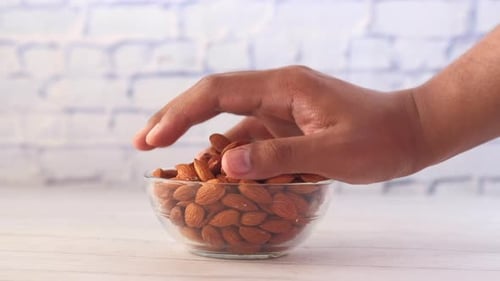 Hand Grabbing Almonds from a Glass Bowl