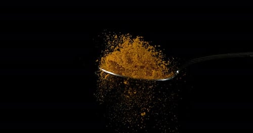 Spoon and Curry Powder falling against Black Background, Slow motion 4K