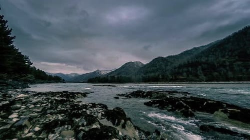 Zeitrafferaufnahme eines Flusses in der Nähe eines Bergwaldes. Riesige Felsen und schnelle Wolkenbewegungen.