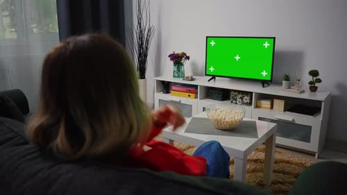 Girl Watching Green Chroma Key Screen TV, Relaxing Sitting on a Couch Home.