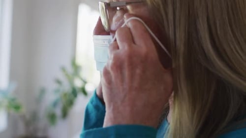 Woman Puts on Blue Surgical Mask Indoors