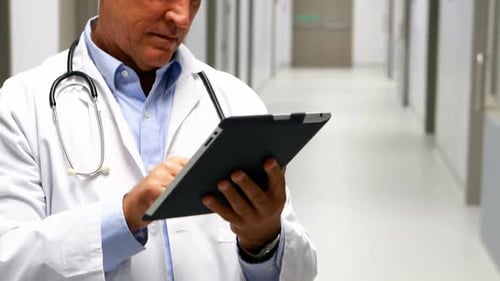 Mature Doctor Working on Tablet in Hospital Hallway