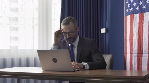 Man Working at Desk in Front of Flag