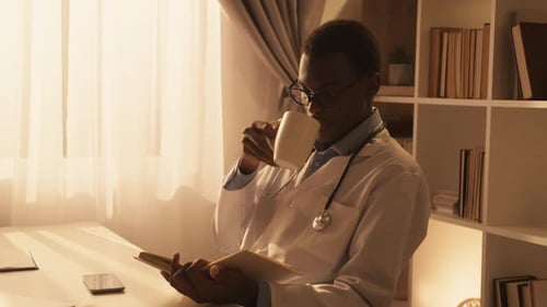 Person in Lab Coat Reading Book and Drinking
