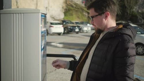 Man Paying Parking Meter with Coins in City
