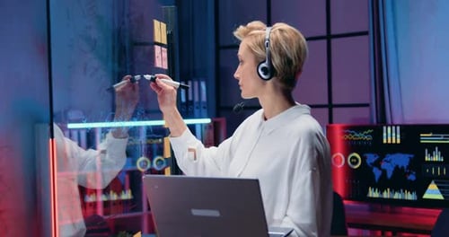 Femme d'affaires au casque prenant des notes sur une planche en verre tout en parlant par chat vidéo