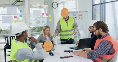 Multiracial Engineers in Hardhats Brainstorming Over joint Building Project During meeting