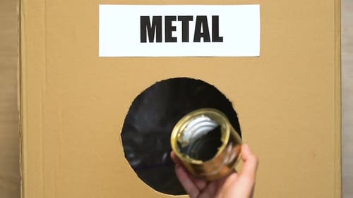 Hand Throwing Used Tin Can Into Metal Container With Plastic Waste on Bottom
