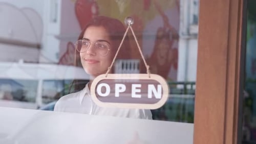 Young Woman Turns Sign to Open on Business Door