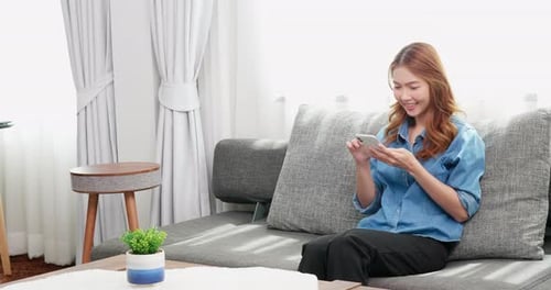 Smiling Young Woman Using Phone on Couch