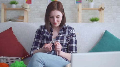 Close Up Woman Sitting on the Couch in Front of a Laptop Learning To Knit