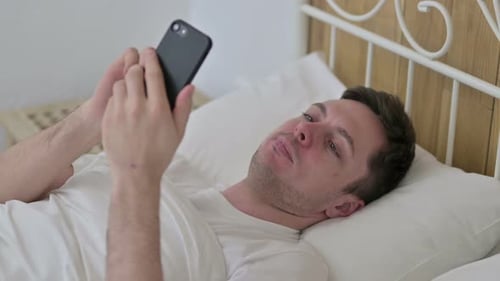 Man Lying in Bed Using Cellphone