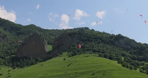 Paragliding Pilots Fly Paragliders Among Clouds and Green Mountains