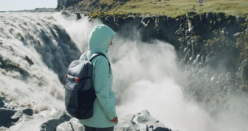 Woman Standing at the Cliff Edge Looking at Detifoss Waterfall in Iceland