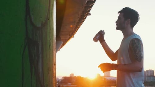 Young Man with Spray Bottle Drawing Graffity Under the Bridge