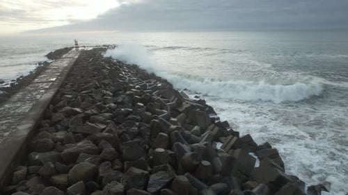 Waves Crashing on Pier and Lighthouse at Sunset