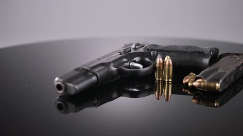 Gun Control. 9mm handgun with bullets rotating on a reflective surface
