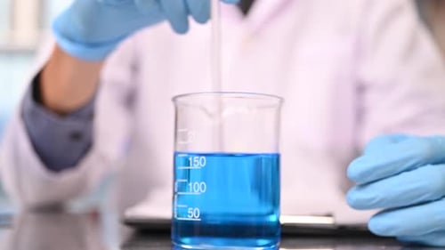 Scientist Adding Liquid to Beaker in Laboratory