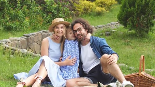 Portrait of Happy Young Family Sitting on Grass in Green Park