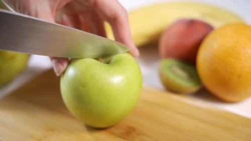 Weibliche Hände schneiden Apfel mit einem Messer auf einem Holzschneidebrett