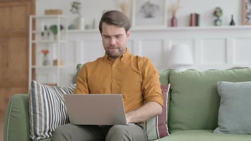 Young Man Looking at Camera while using Laptop in Office