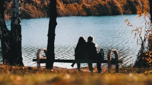 Young Romantic Couple Sitting on a Bench in an Autumn Park By the River