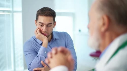 Closeup View From Back of Mature Grayhaired Doctor to Sad Male Patient Explaining Problem Sitting at