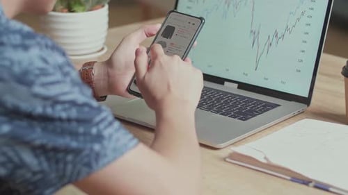 Young Adult Analyzing Data on Smartphone and Laptop