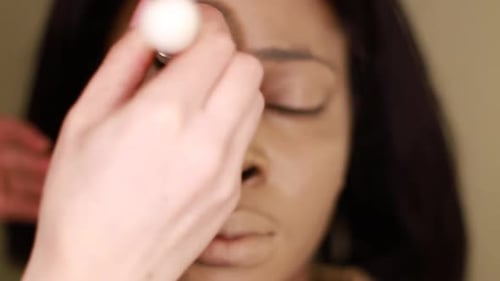 A female makeup artist applying gold makeup to a black African-American model.
