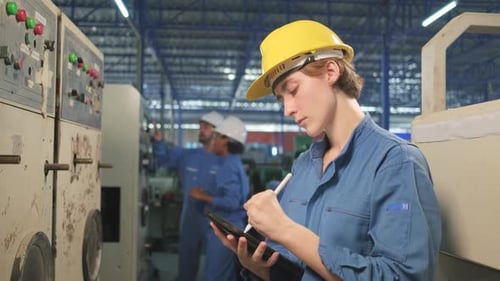 Female engineer inspects machine's control panel in manufacture factory.