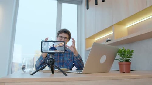 Young male blogger writing online blog, podcast at home using smartphone
