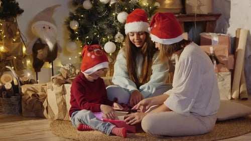 Family Opens Christmas Presents Together by Glowing Tree