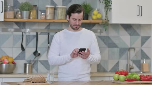 Man Using Cellphone in Kitchen at Home