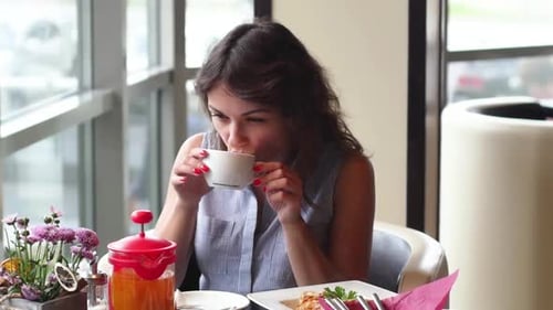 Young Brunette Is Drinking Tea in a Cafe. Woman Eating Breakfast in a Cafe.