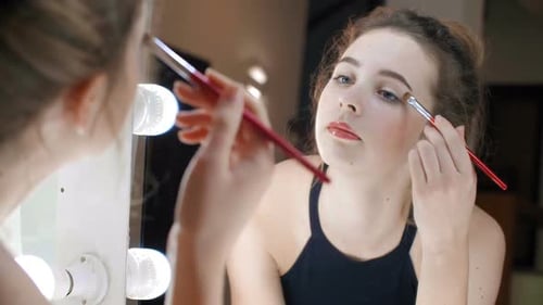 Woman Applying Eye Shadow in Front of Lighted Mirror