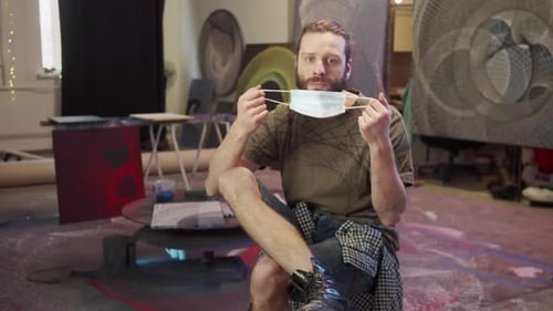 Bearded Man Removes Mask and Smiles in Art Studio