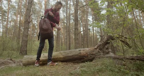 Man with Backpack Rests on Log in Forest