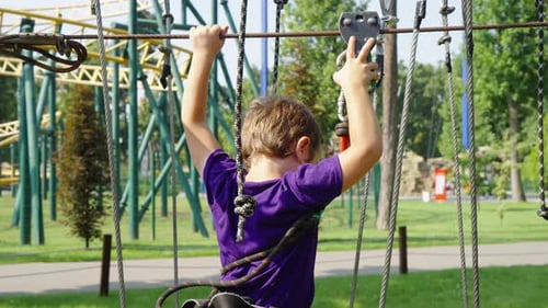 Boy Moving Safety Harness on Rope Trail in Amusement Park