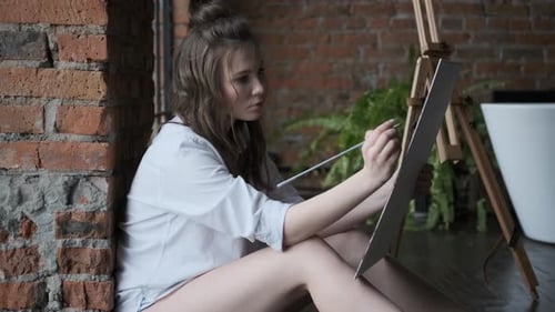 Artist Paints a Picture in a Home Studio in the Style of a Loft. Portrait of an Attractive Girl