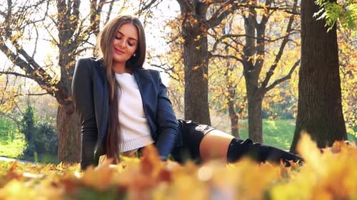 Young Beautiful Woman Lies on the Foliage in Autumn Park and Smiles To Camera