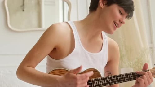 Young woman playing on ukulele practicing music guitar and sing at home.