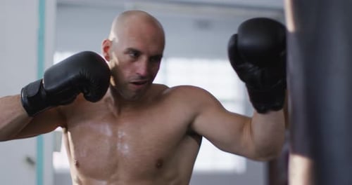 Caucasian male trainer wearing boxing gloves training with punching bag at the gym