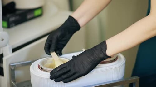 Gloved Hands Stirring Wax for Beauty Treatment