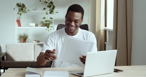Young Adult Reviews Paperwork at Home Office Desk