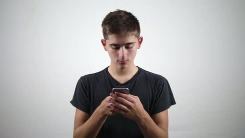 An Attractive Young Man Uses a Phone and Smiles Against a White Background. Medium Shot