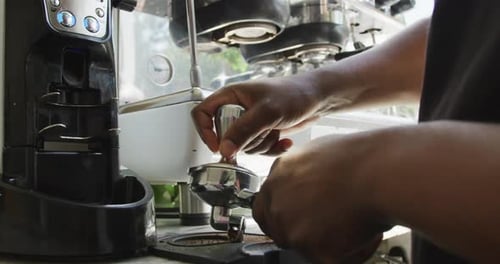 Close up of african american male barista making coffee using coffe machine at cafe