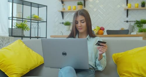 Woman Is Making Online Payment Holding Bank Card Using Modern Laptop at Home Sitting on Sofa and