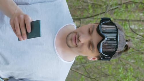 Young Adult With Goggles Holds Phone Outside