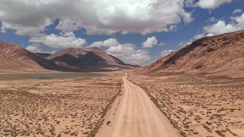 Aerial Over Gravel Off Road Trail Near Arid Desert Mountains in Sunny Day